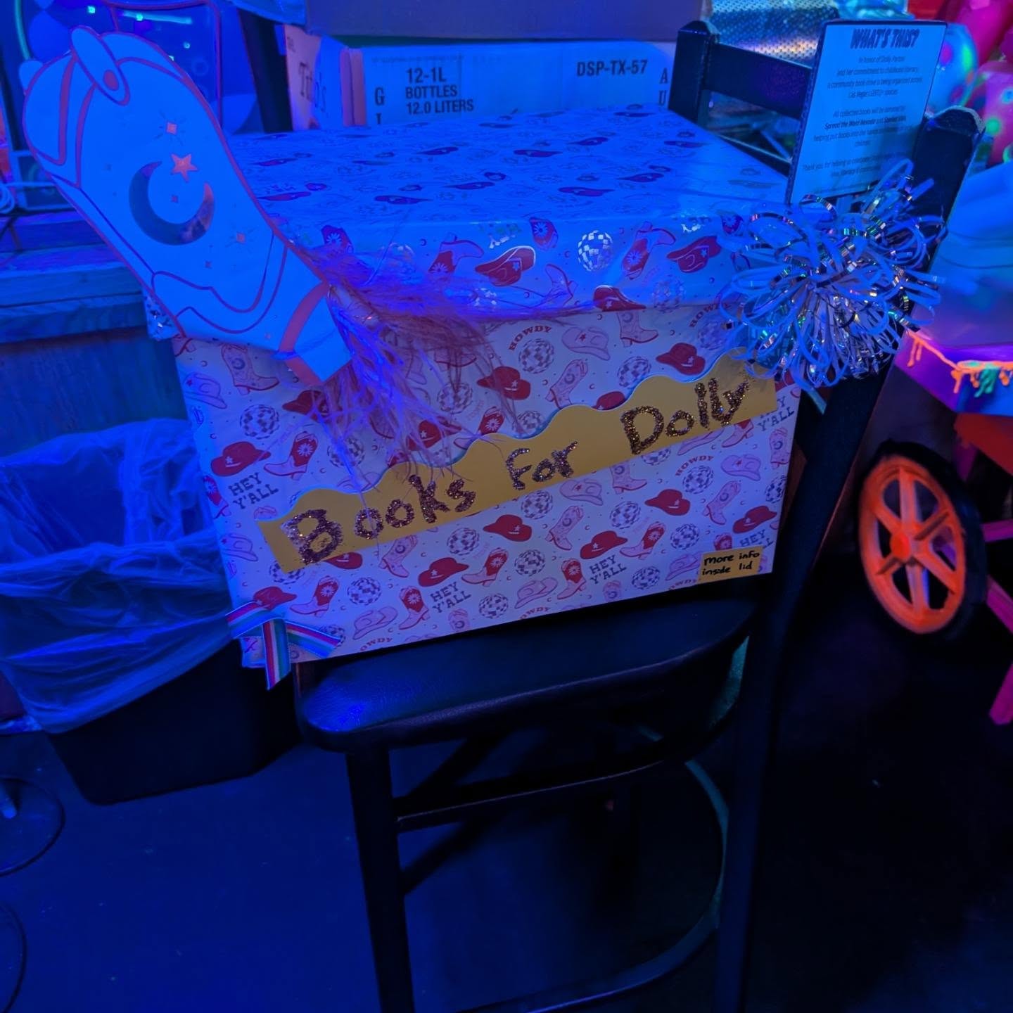 A handmade Books for Dolly donation box at The Phoenix Bar & Lounge under blue and pink bar lights